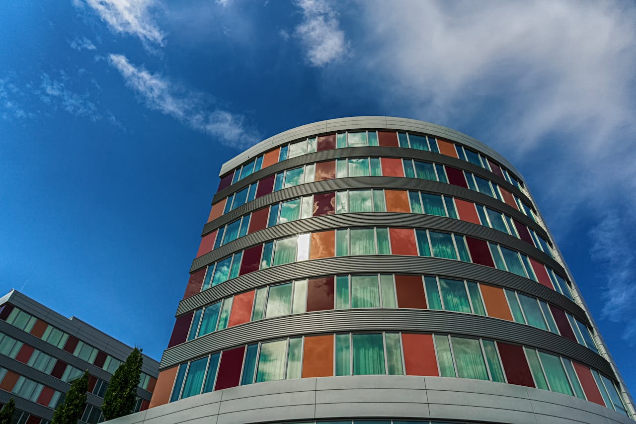 A modern curved building with colorful panels against a blue sky, showcasing urban architecture.
